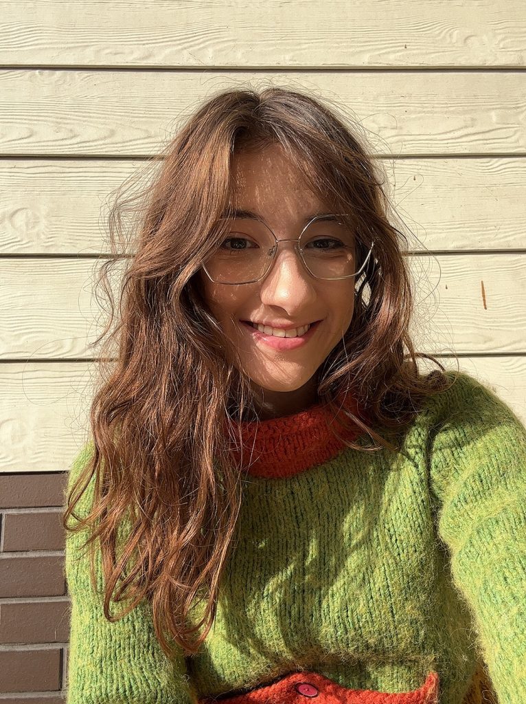 Frankie wearing a green and orange knitted jumper, smiling at the camera in a relaxed selfie.
